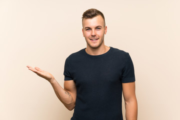Young handsome blonde man over isolated background holding copyspace imaginary on the palm to...