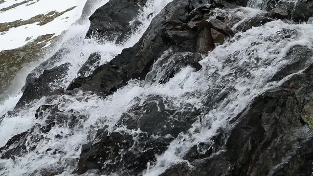 Beautiful waterfal over the valley near the Susch pass near Davos in Swizerland surrounded by snow. Filmed in slow motion in June.