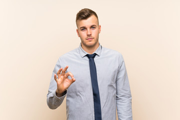 Young blonde businessman over isolated background showing an ok sign with fingers