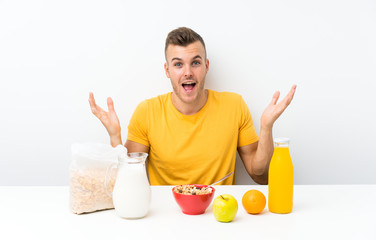 Young blonde man having breakfast with surprise facial expression
