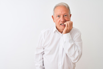 Senior grey-haired man wearing elegant shirt standing over isolated white background looking stressed and nervous with hands on mouth biting nails. Anxiety problem.