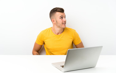 Young blonde man in a table with a laptop laughing and looking up