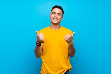Young man with yellow shirt over isolated blue background with thumbs up gesture and smiling