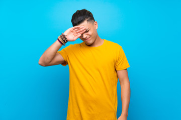 Young man with yellow shirt over isolated blue background with tired and sick expression