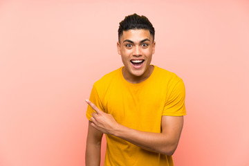 Young man with yellow shirt over isolated pink wall pointing finger to the side