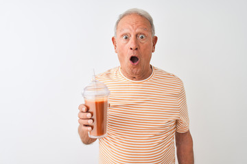 Senior man wearing striped t-shirt drinking tomato smoothie over isolated white background scared in shock with a surprise face, afraid and excited with fear expression