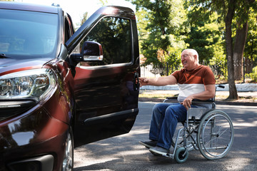 Senior man in wheelchair opening door of his van outdoors © New Africa