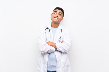 Young doctor man over isolated white wall looking up while smiling