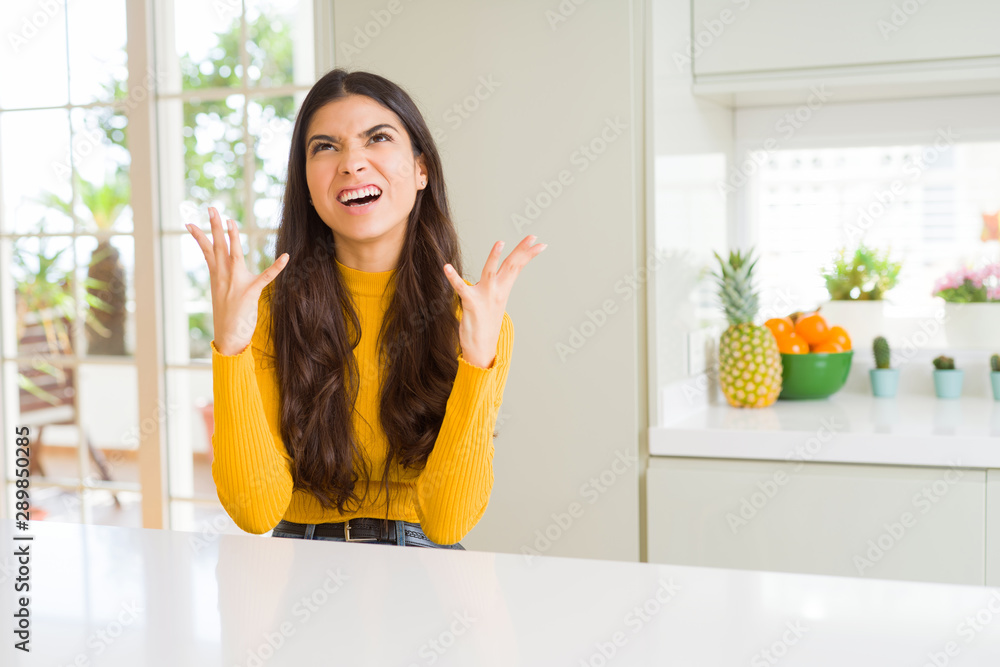 Sticker young beautiful woman at home on white table crazy and mad shouting and yelling with aggressive expr