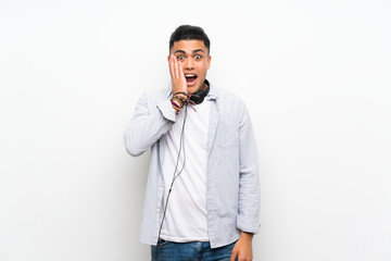 Young man over isolated white wall with earphones with surprise and shocked facial expression