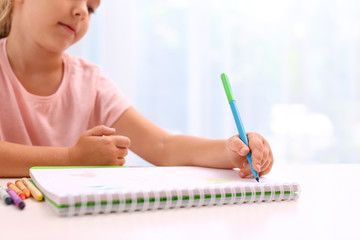 Little left-handed girl drawing at table in room, closeup