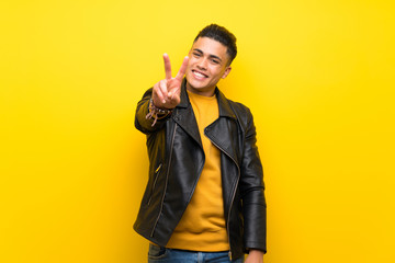 Young man over isolated yellow background smiling and showing victory sign