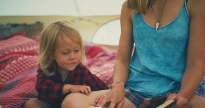 Young mother reading book with toddler in tent