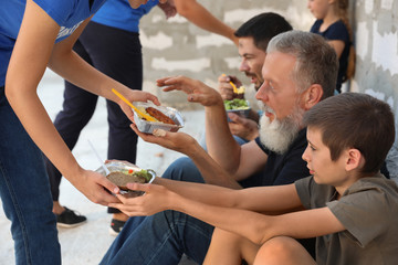 Poor people receiving food from volunteers near wall outdoors