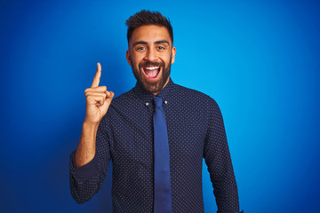 Young indian businessman wearing elegant shirt and tie standing over isolated blue background...