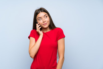 Brunette young woman with a mobile phone over isolated blue wall