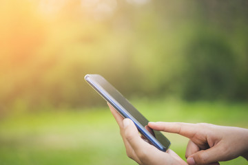 Woman hand using smart phone at outdoor nature park with sunset sky abstract background.