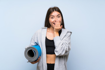Young sport girl with mat over isolated blue background with surprise facial expression