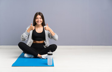 Fototapeta premium Young sport woman sitting on the floor with mat giving a thumbs up gesture