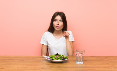 Young woman with a salad surprised and pointing front