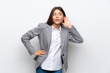 Young business woman over isolated white background listening to something by putting hand on the ear