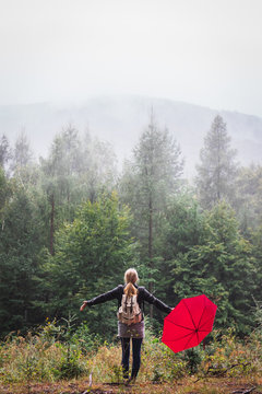 Bad weather can not ruin her happy day. Woman with red umbrella standing in rain and fog at forest