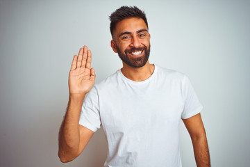 Young indian man wearing t-shirt standing over isolated white background Waiving saying hello happy and smiling, friendly welcome gesture © Krakenimages.com