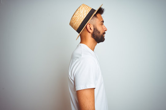 Young indian man on holiday wearing summer hat standing over isolated white background looking to side, relax profile pose with natural face with confident smile.