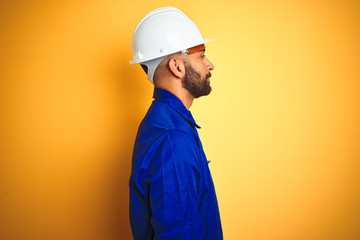 Handsome indian worker man wearing uniform and helmet over isolated yellow background looking to...