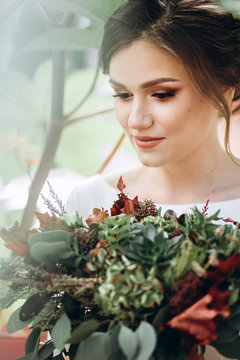 Portrait of a beautiful bride in a modest dress. Young brunette girl in a white dress with long sleeves. Cute bride with an autumn bouquet. Closeup portrait of a woman outdoors in autumn street.