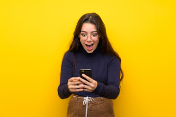Teenager girl over isolated yellow wall surprised and sending a message