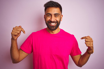 Young indian man wearing t-shirt standing over isolated pink background looking confident with...