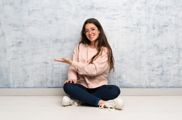 Teenager student girl studying in a table presenting an idea while looking smiling towards