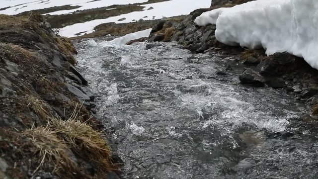 Small river in the valley at the Susch pass near Davos in Switzerland surrounded by snow. Shot was filmed in slow motion in June.