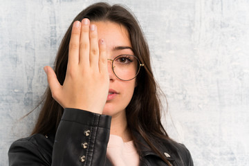 Teenager girl over grunge wall covering a eye by hand