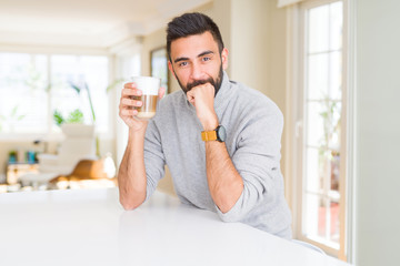 Handsome hispanic man drinking a cup of coffee serious face thinking about question, very confused idea