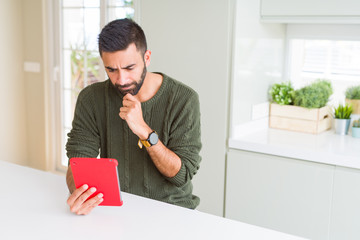 Handsome hispanic man using tablet at home serious face thinking about question, very confused idea