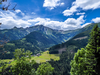 Obraz premium A stunning view on Alpine valley. Hiking trails in the high mountain. Green grass and bushes cover the slopes. A remote view on small settlement in the bottom of the valley. Spring in the mountains.