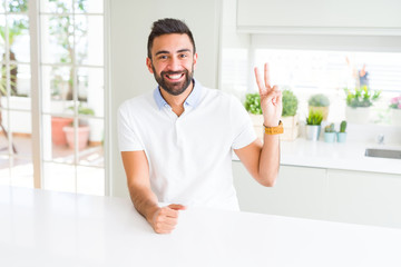 Handsome hispanic man casual white t-shirt at home smiling with happy face winking at the camera doing victory sign. Number two.