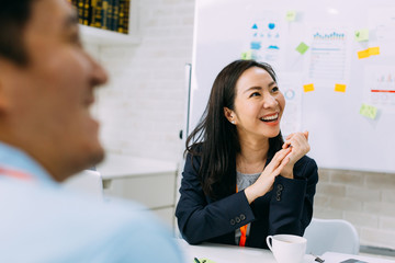 Asian mature business woman smiling and looking at other business people while sitting in meeting....