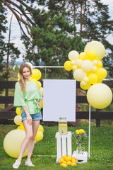 Young adult beautiful blonde girl happy on green grass with balloons and lemonade