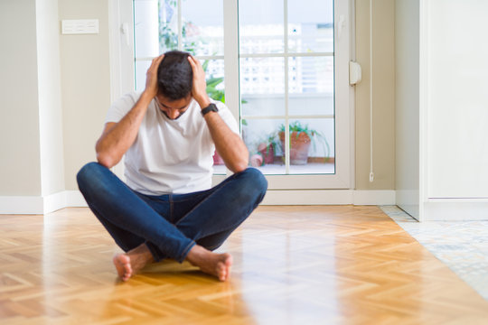 Handsome hispanic man wearing casual t-shirt sitting on the floor at home suffering from headache desperate and stressed because pain and migraine. Hands on head.