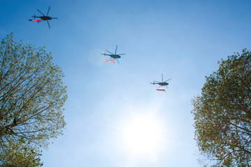 Three gray military helicopters fly in the blue sky. They carry flags with them. Demonstration of a peaceful flight. Day of the city. Memory. Background with copy space for text. Air show