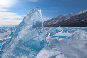 Large glowing transparent blue ice block among glacier field on mountains background, beautiful winter natural landscape