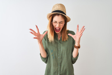 Obraz na płótnie Canvas Redhead woman wearing green shirt glasses and hat over isolated white background celebrating mad and crazy for success with arms raised and closed eyes screaming excited. Winner concept