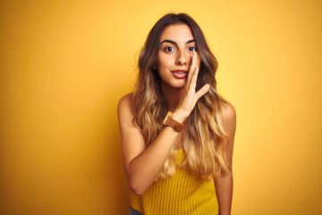 Young beautiful woman wearing t-shirt over yellow isolated background hand on mouth telling secret...