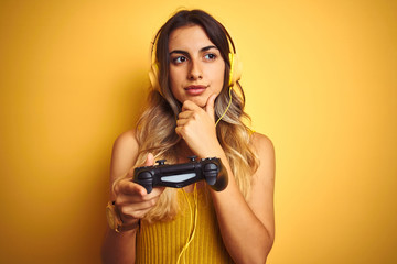 Young beautiful woman playing video game using gamepad over yellow isolated background serious face...