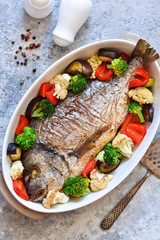 Baked dorado with different vegetables and basil on a concrete background. View from above.