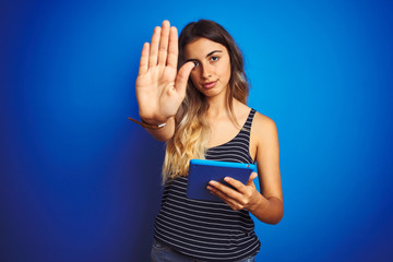 Young beautiful woman using touchpad tablet over blue isolated background with open hand doing stop sign with serious and confident expression, defense gesture