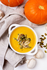 White Bowl of Tasty Pumpkin and Mushrooms Soup with Cream and Pumpkin Seeds on Linen Napkin White Wooden Background Top View Vertical